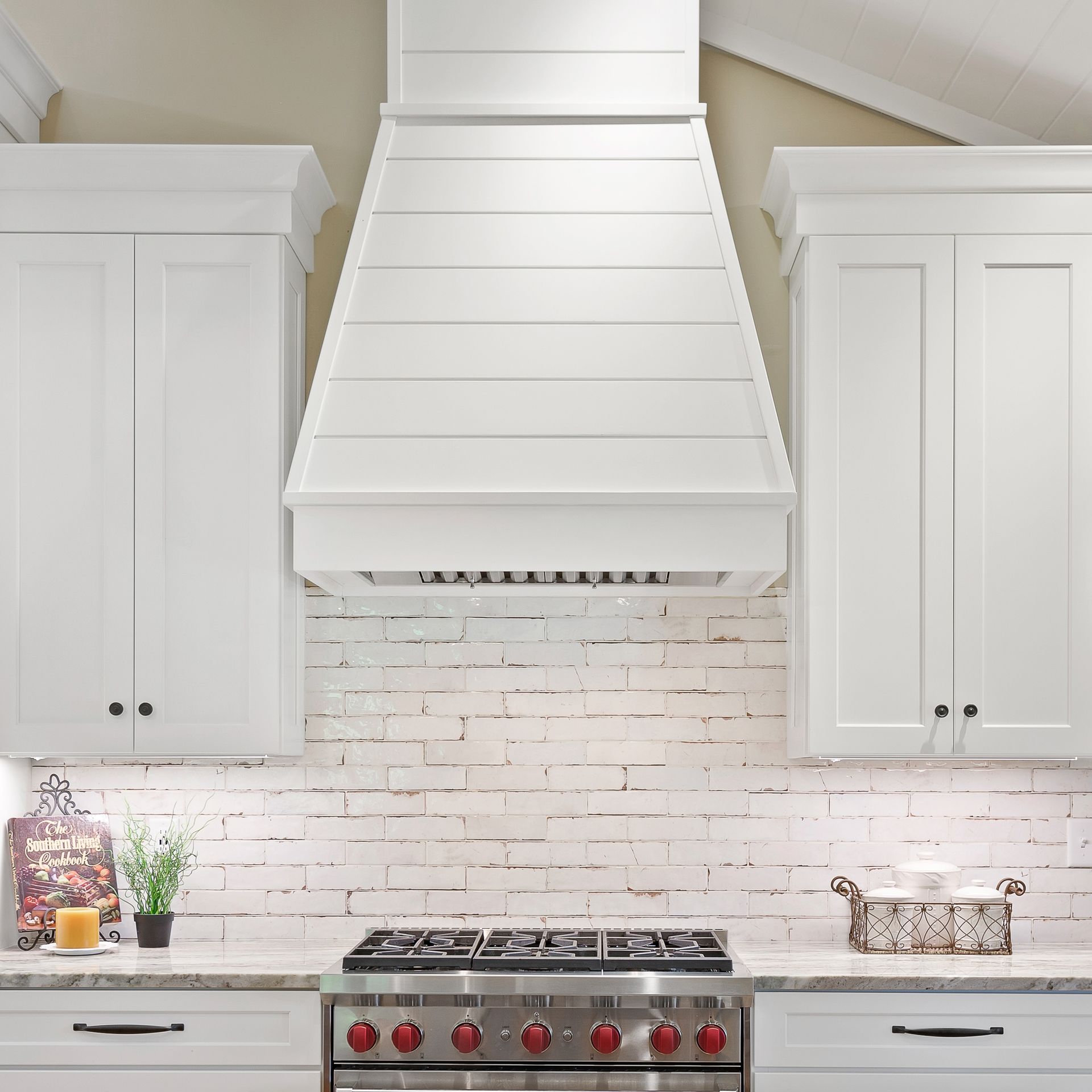 White kitchen with large range hood, subway tile backsplash, and stainless steel stove with red knobs