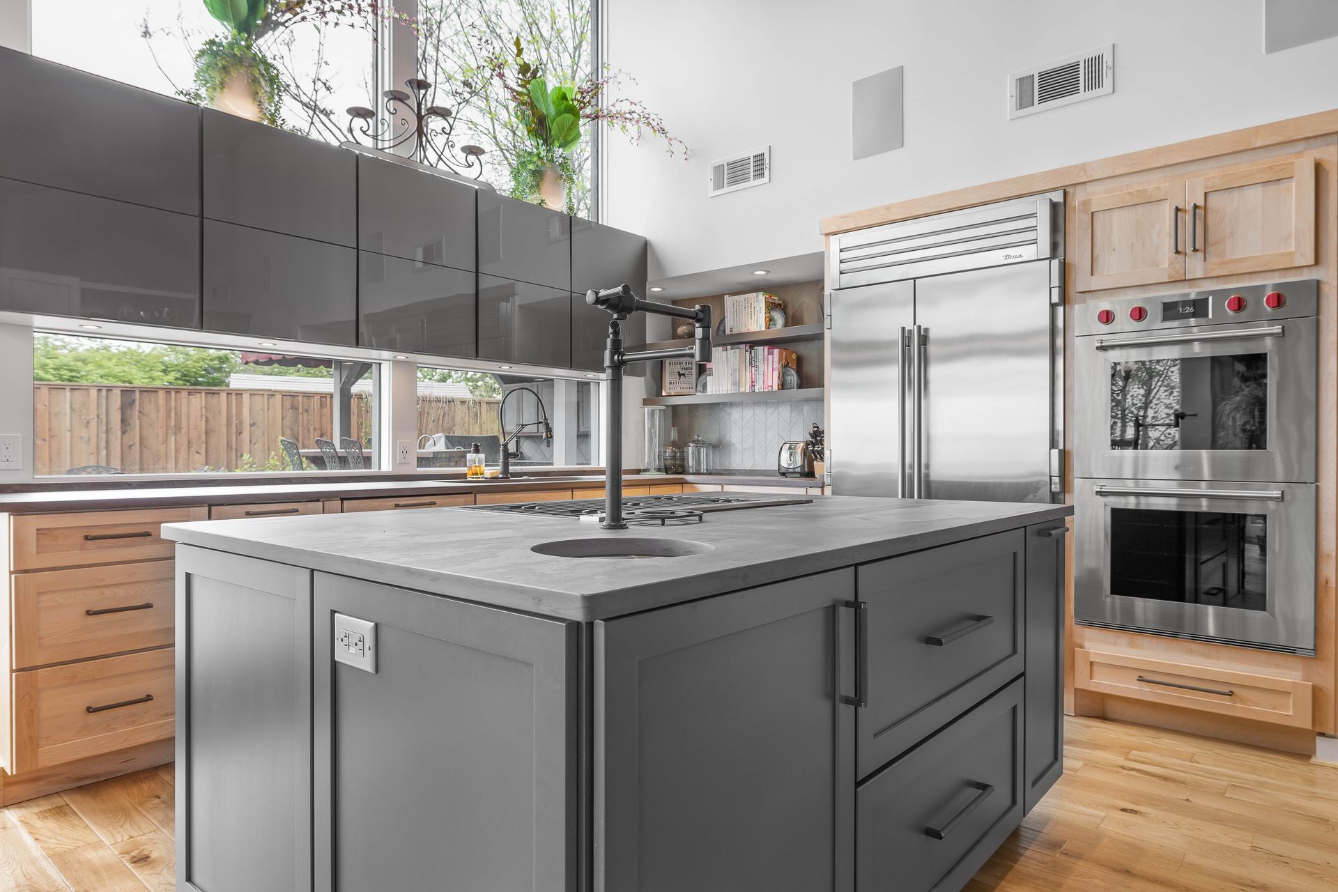 Modern kitchen with gray island, light wood cabinets, and stainless steel appliances.
