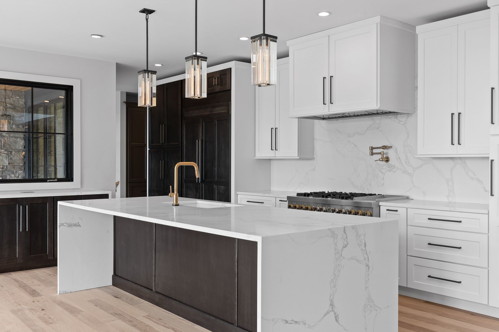 Modern kitchen with white cabinets, dark island, brass faucet, and pendant lights.