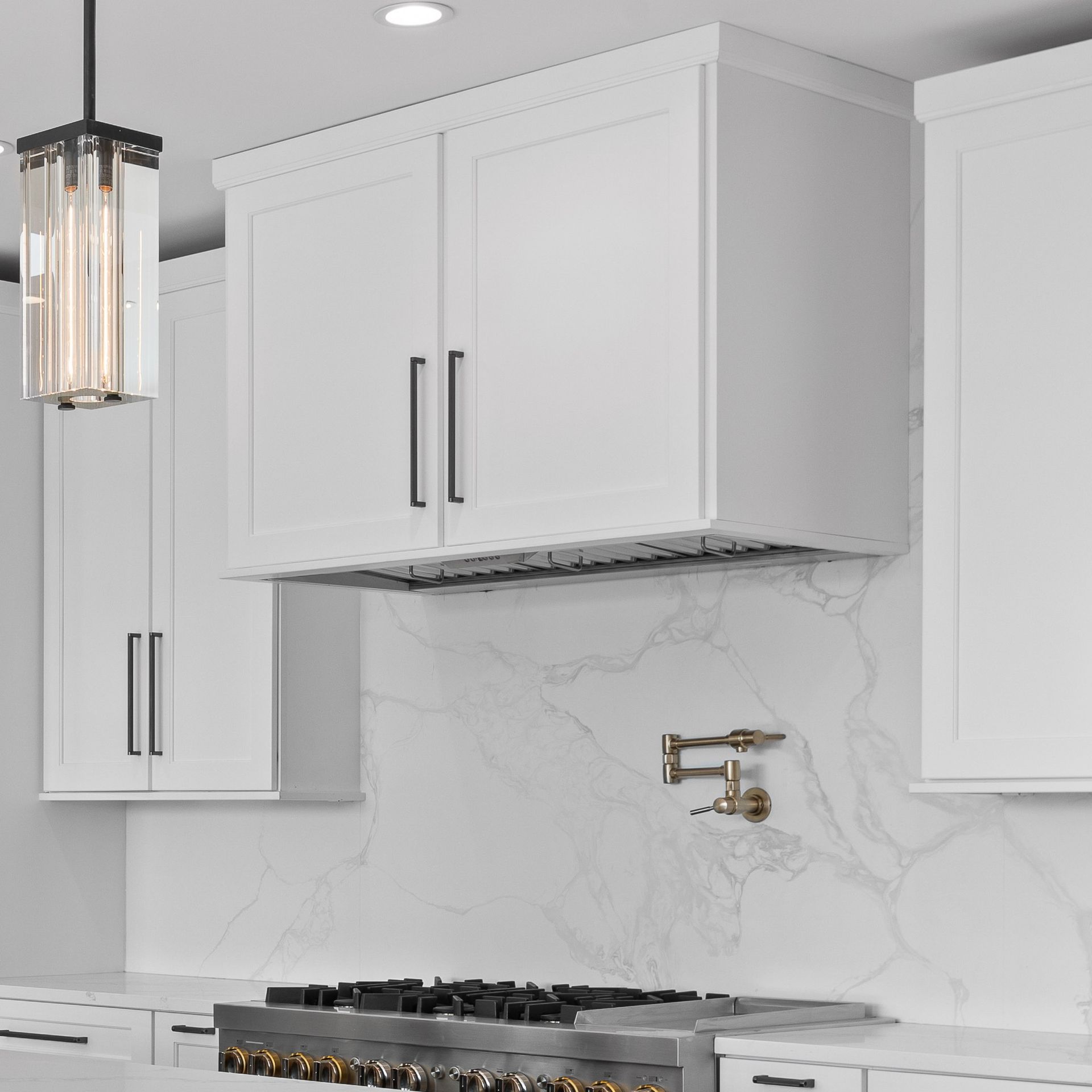 Modern white kitchen with cabinets, marble backsplash, gas range, and brass faucet