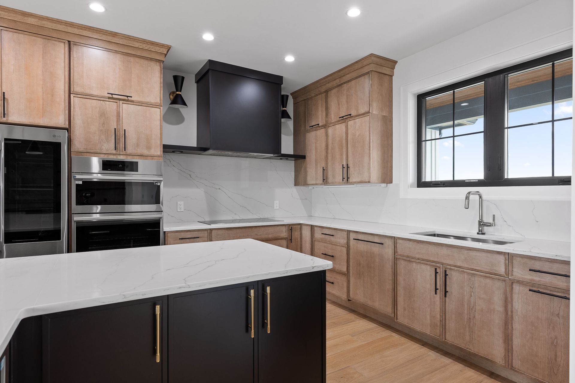 Modern kitchen with light wood cabinets, black island and hood, white countertops.