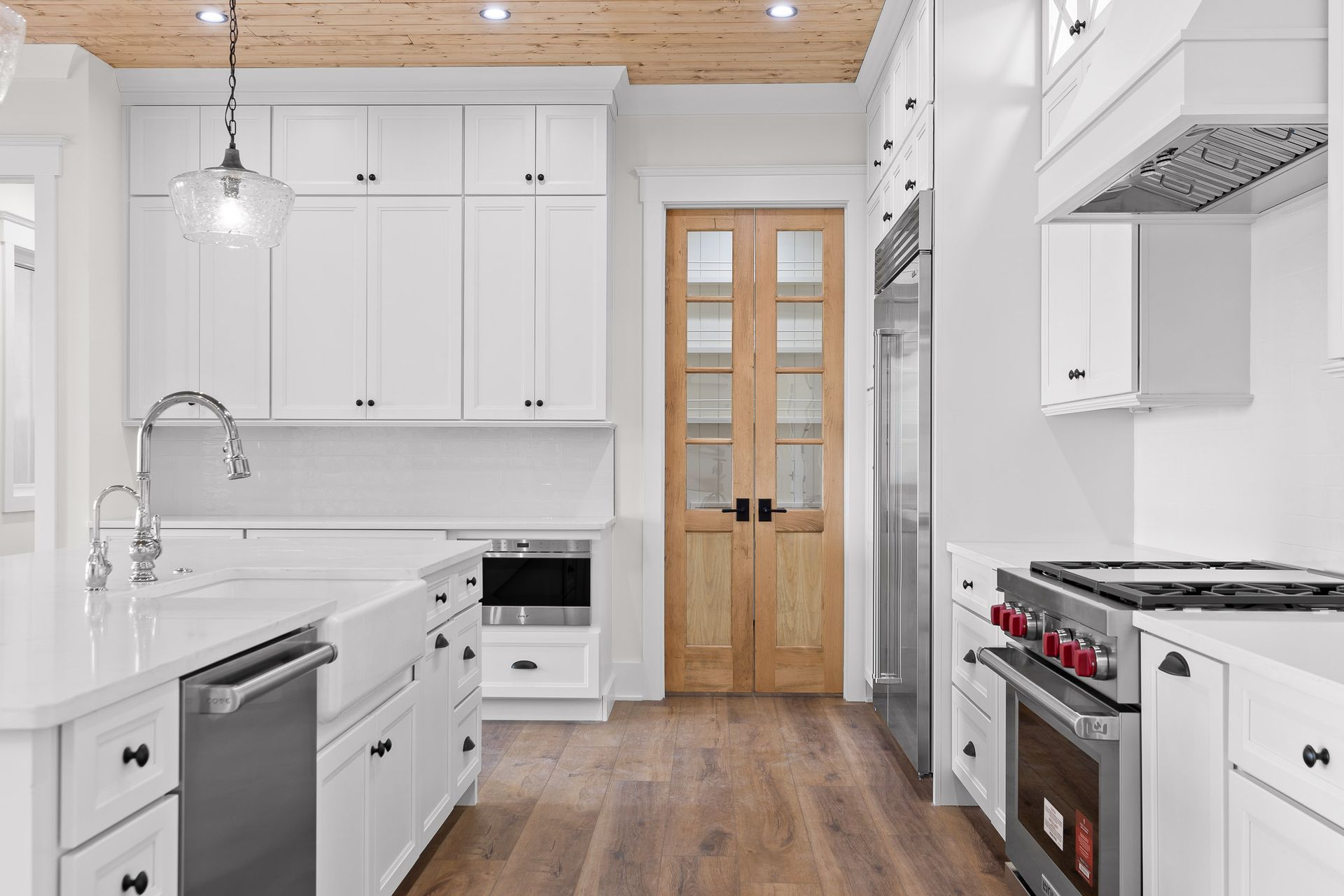 White kitchen with island, cabinets, stainless steel appliances, and wood floor. Wooden double doors.