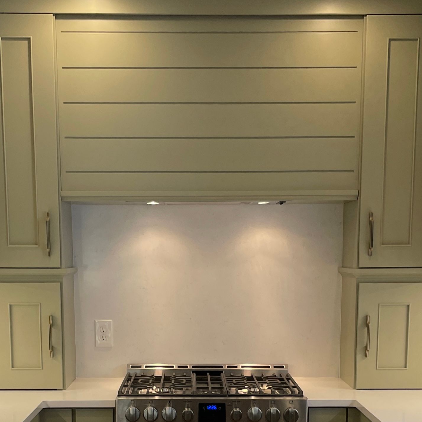 Kitchen stove area with beige cabinets and a lighted backsplash behind a gas cooktop