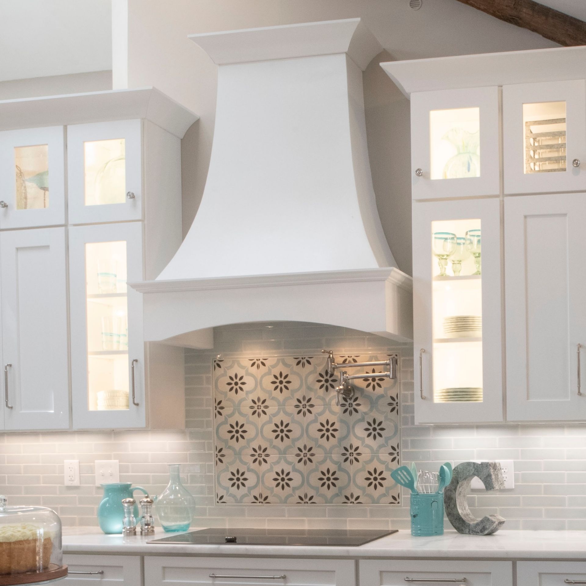 Bright white kitchen with a decorative range hood, tiled backsplash, and countertop accessories
