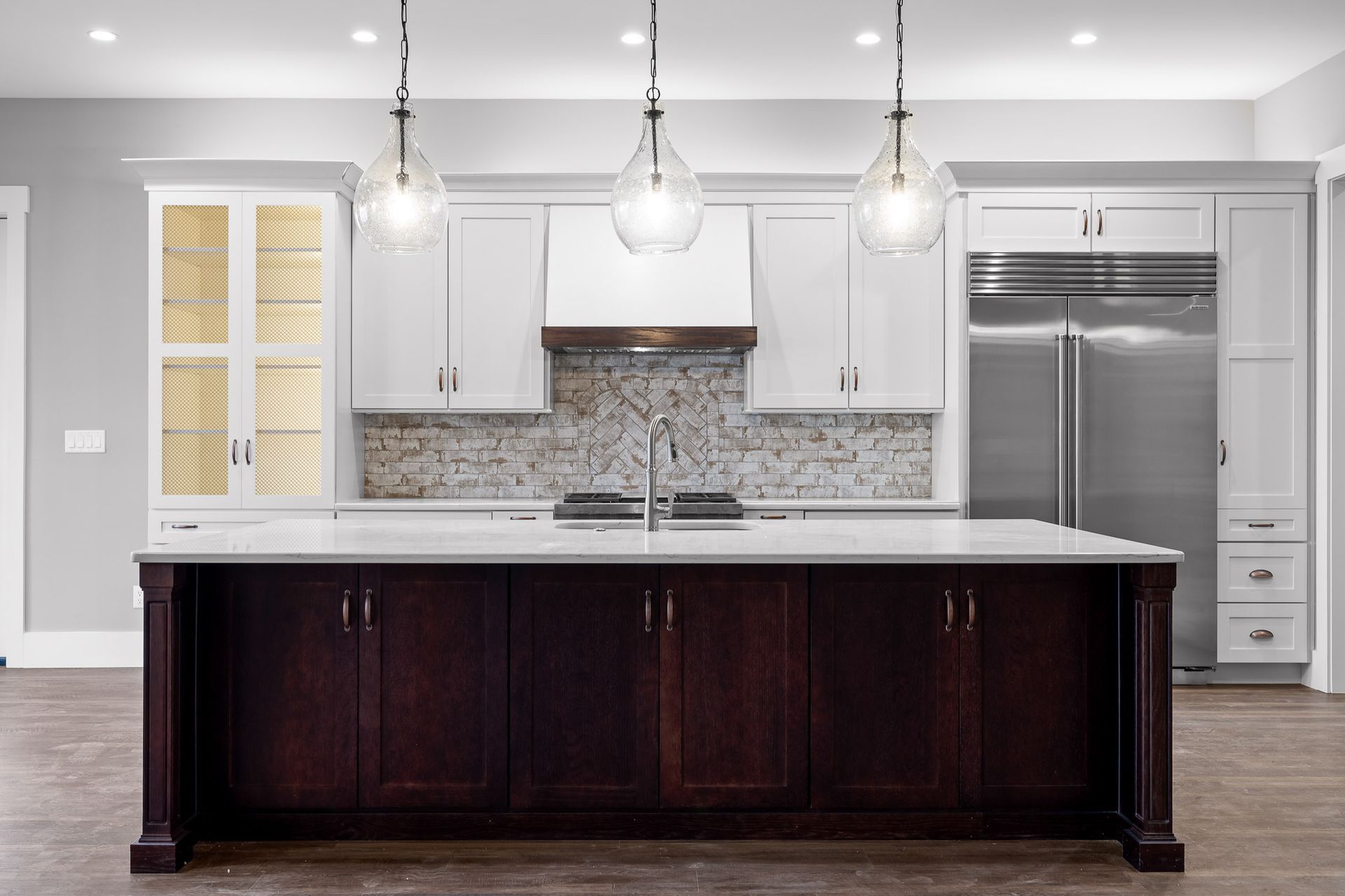 Modern kitchen with white cabinets, dark island, and pendant lights.