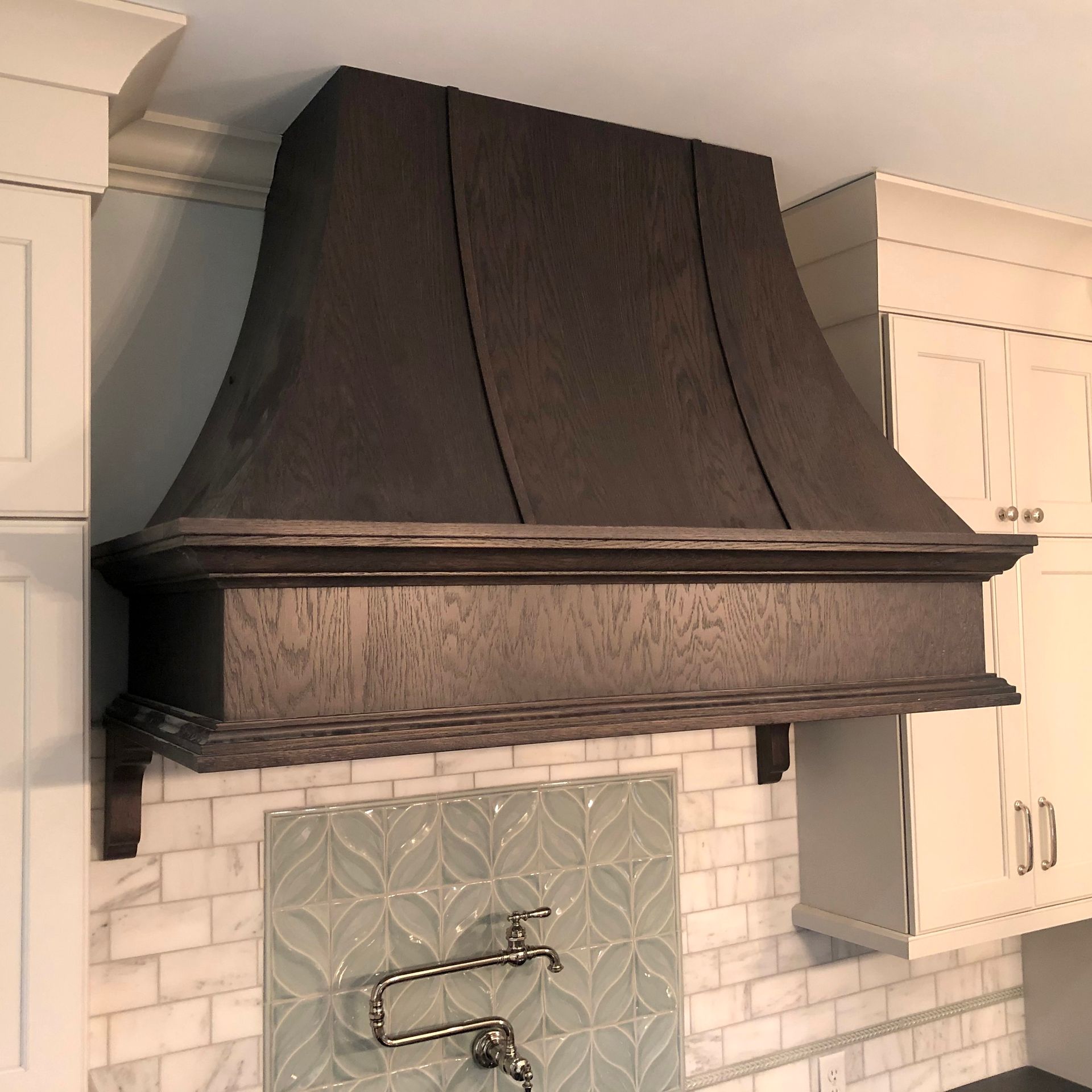 Dark range hood above a tiled kitchen backsplash between white cabinets