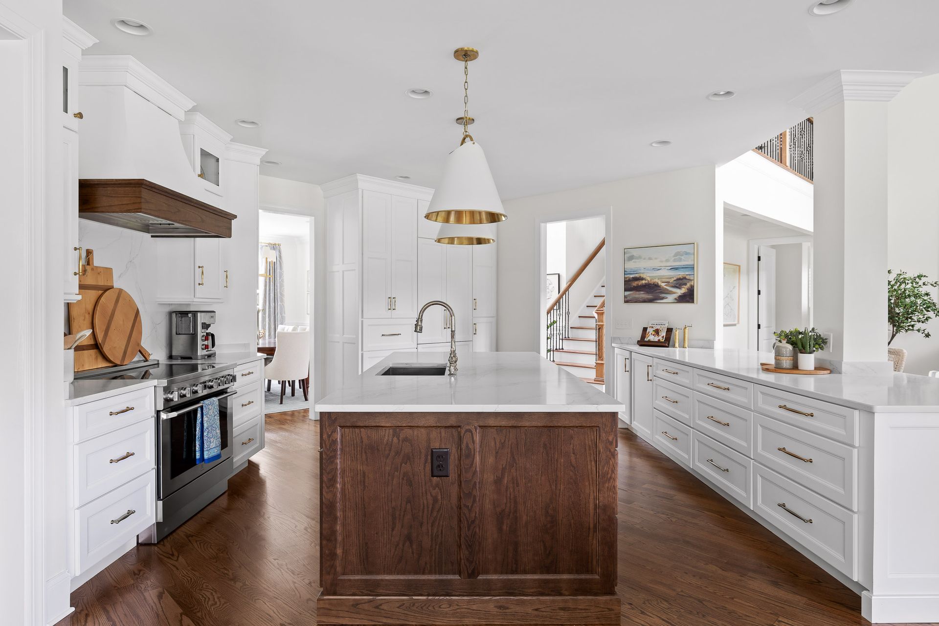 Modern kitchen with white cabinets, dark wood island, gold pendant light, and wood flooring.