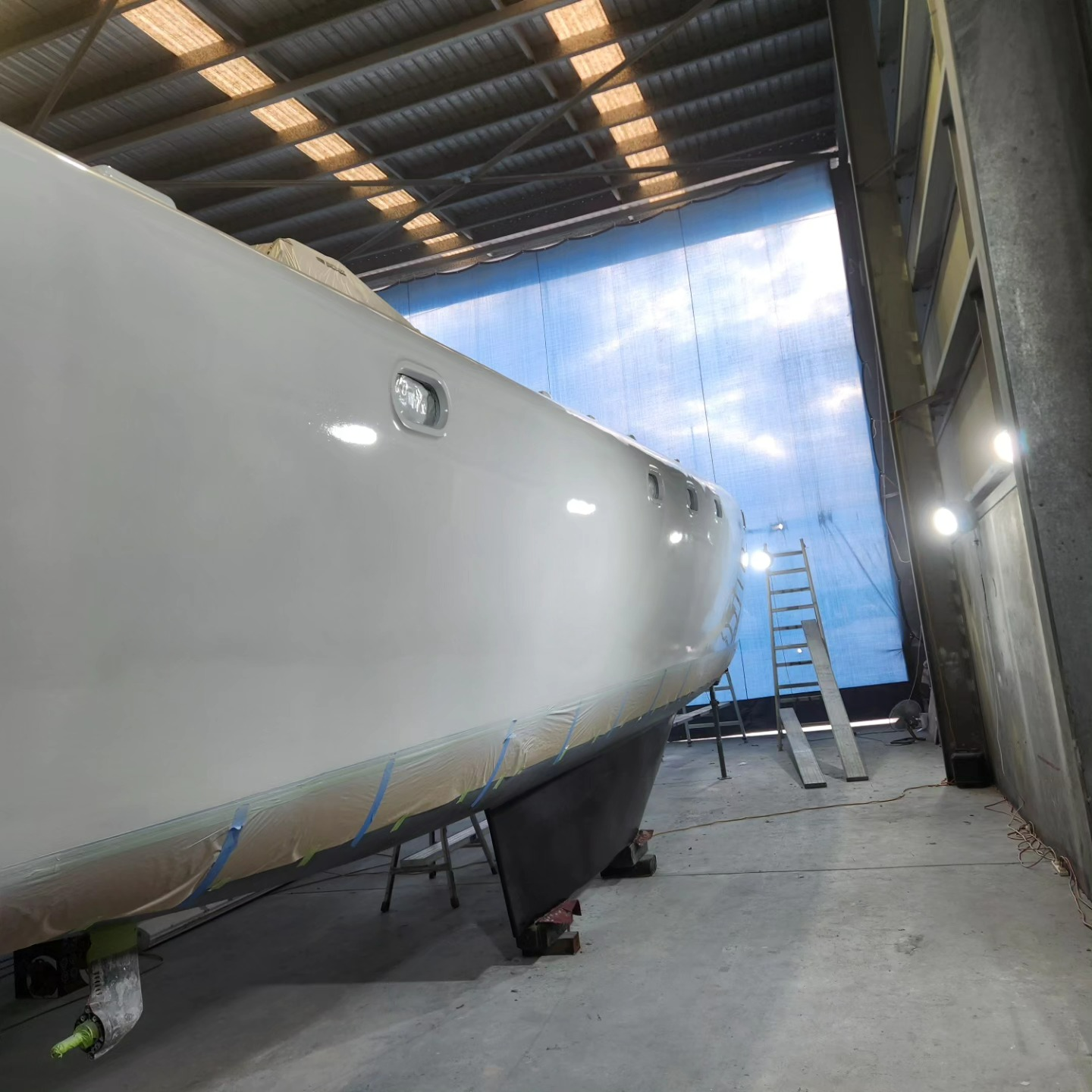 A Boat is Being Painted in a Garage With a Blue Curtain Behind It — Baran Yachting in Sunshine Coast, QLD