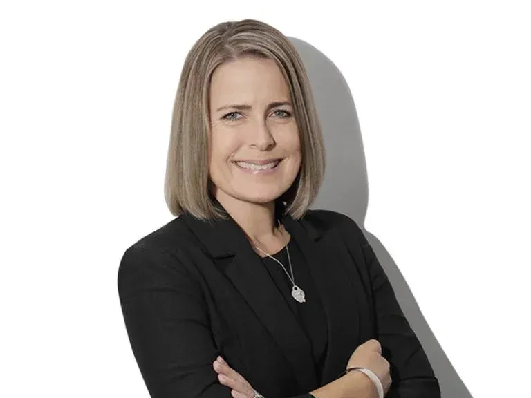 Portrait of a smiling professional in a black blazer with arms crossed against a light background