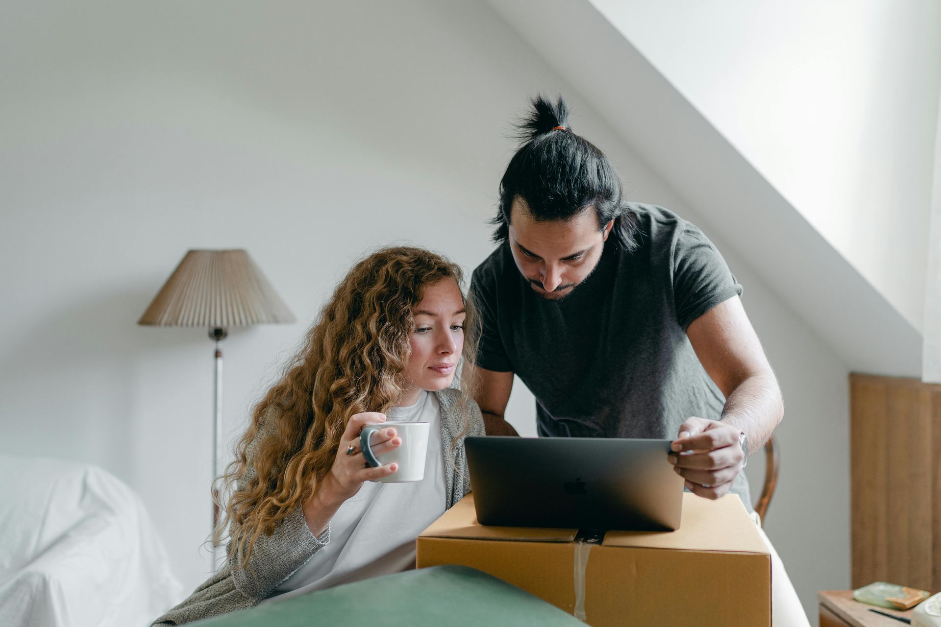 Two people reviewing a laptop while seated in a bed under a slanted ceiling