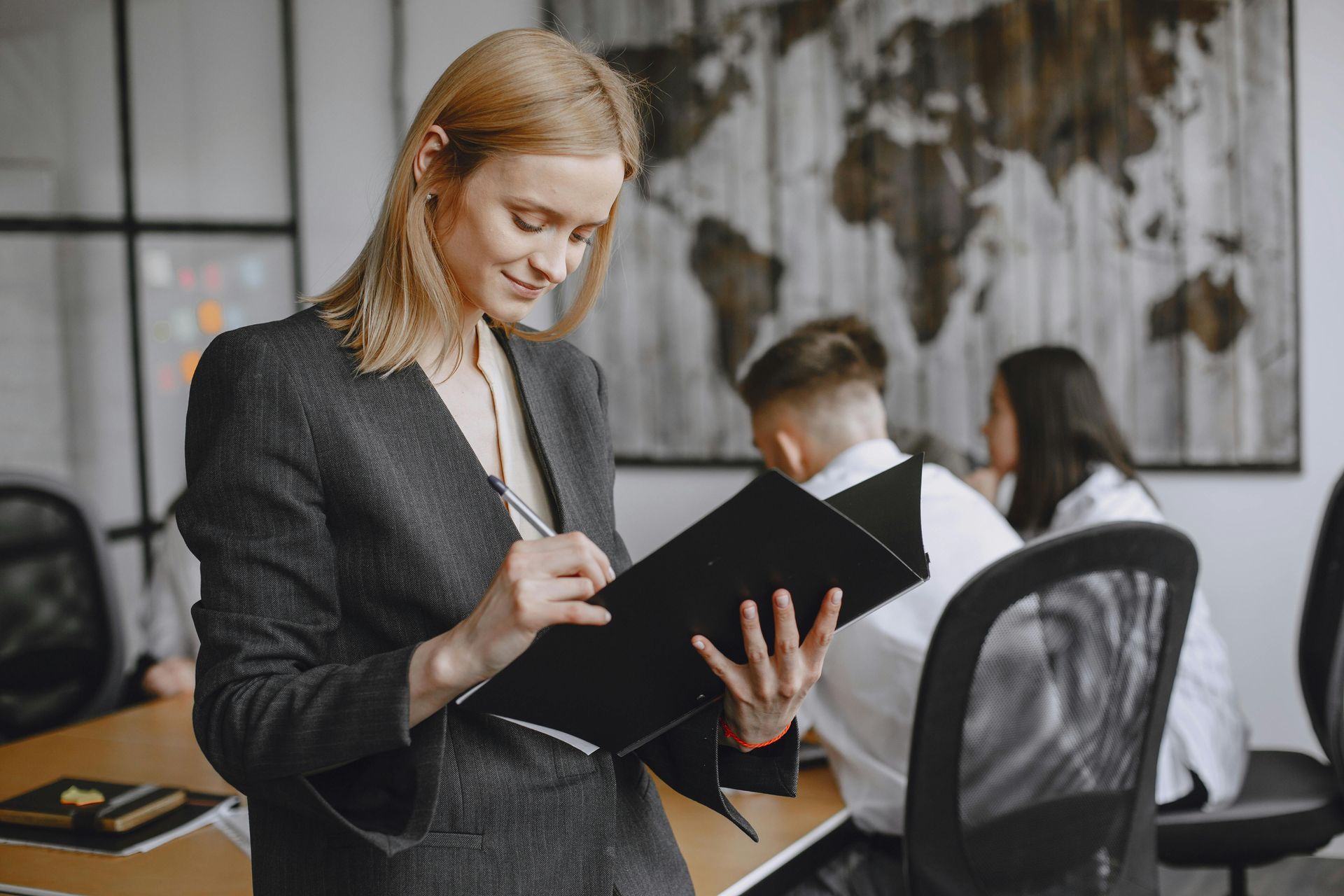 Woman in a dark blazer writing on a clipboard in an office meeting room