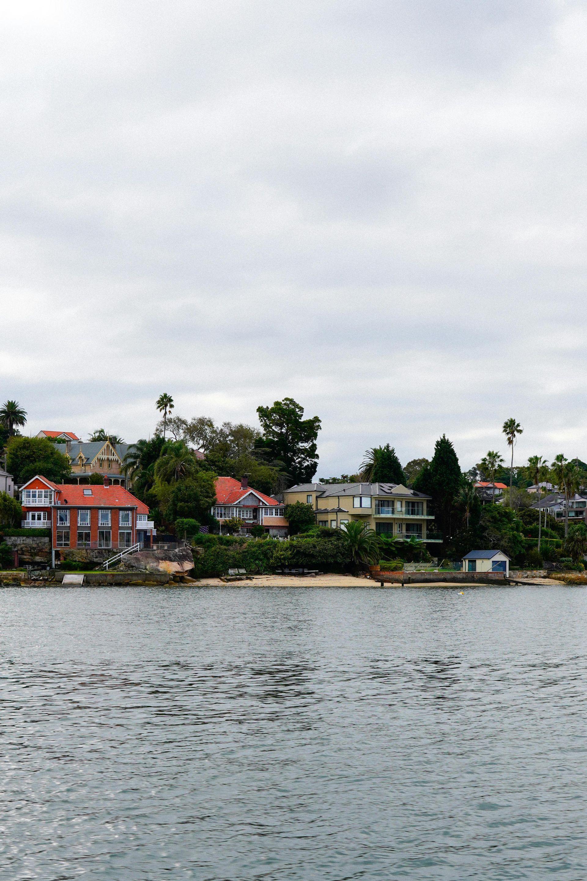 Waterfront homes with red roofs along a shoreline under an overcast sky