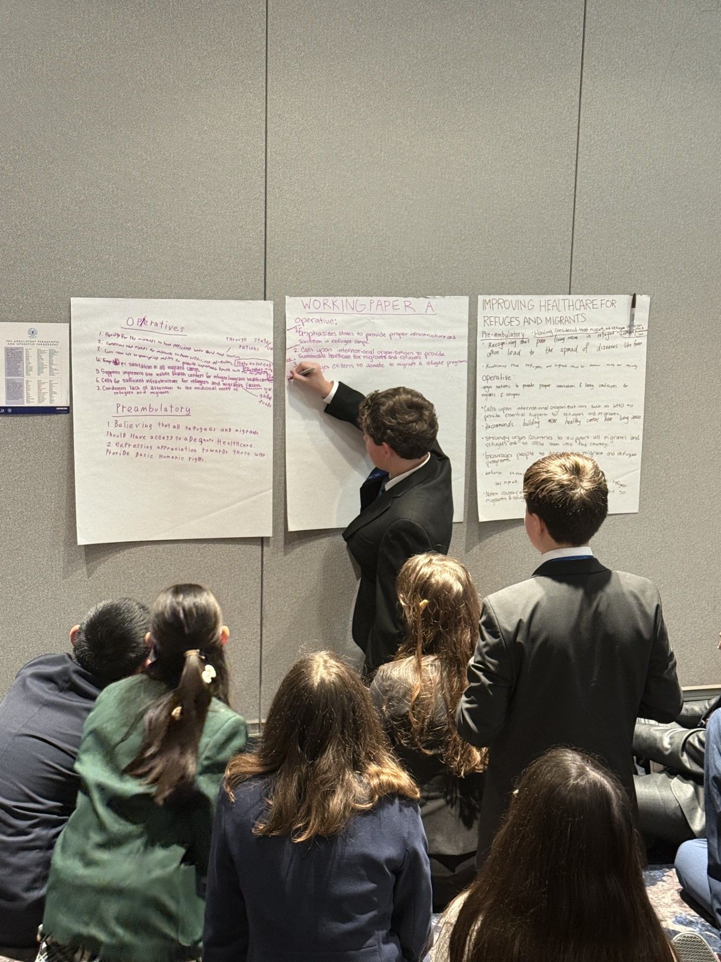 Boy writing on a large notepad in front of his committee members.