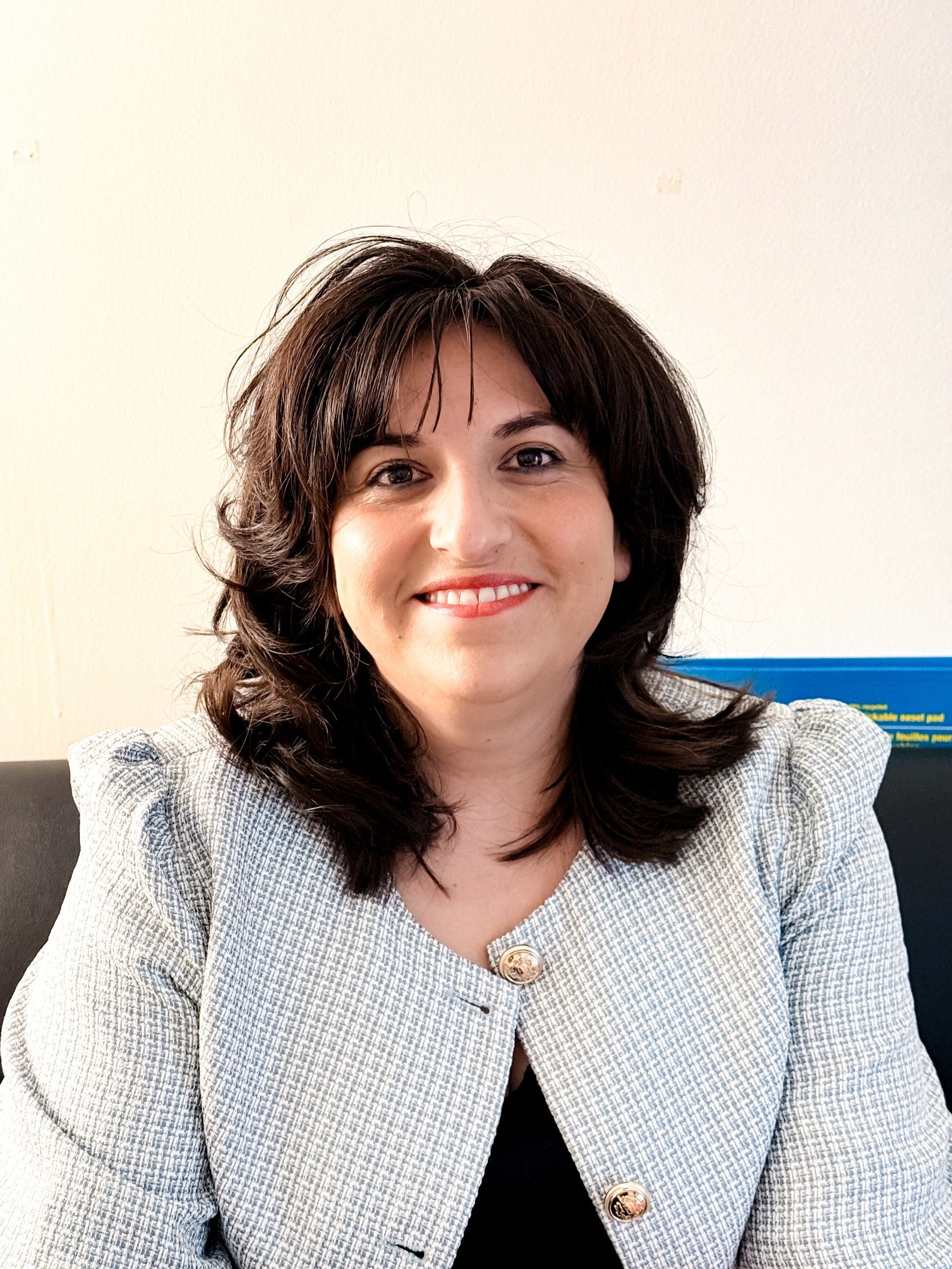Woman in cream blazer and black top sitting on a couch.