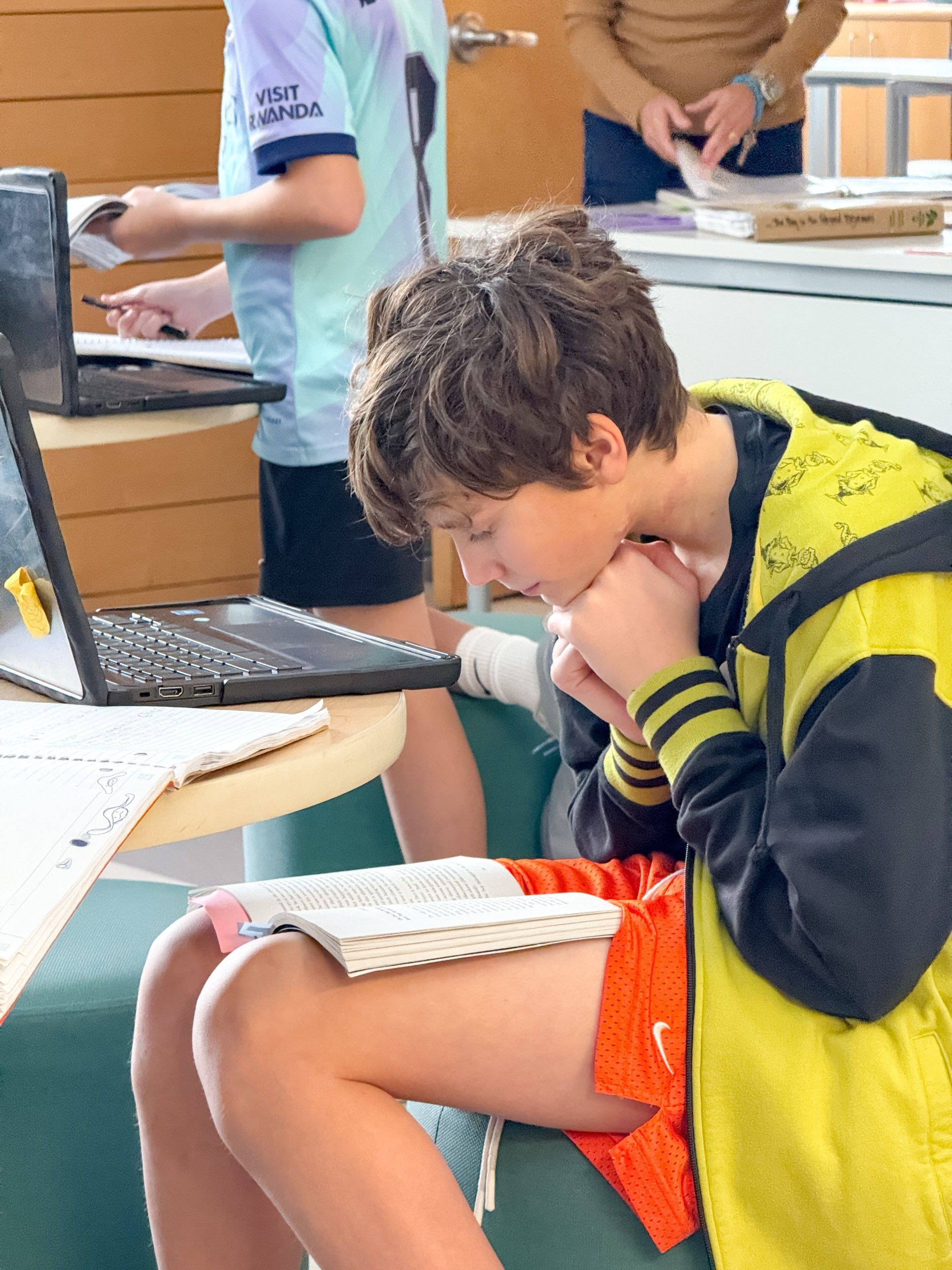 Child working at his computer while searching through text in a novel.