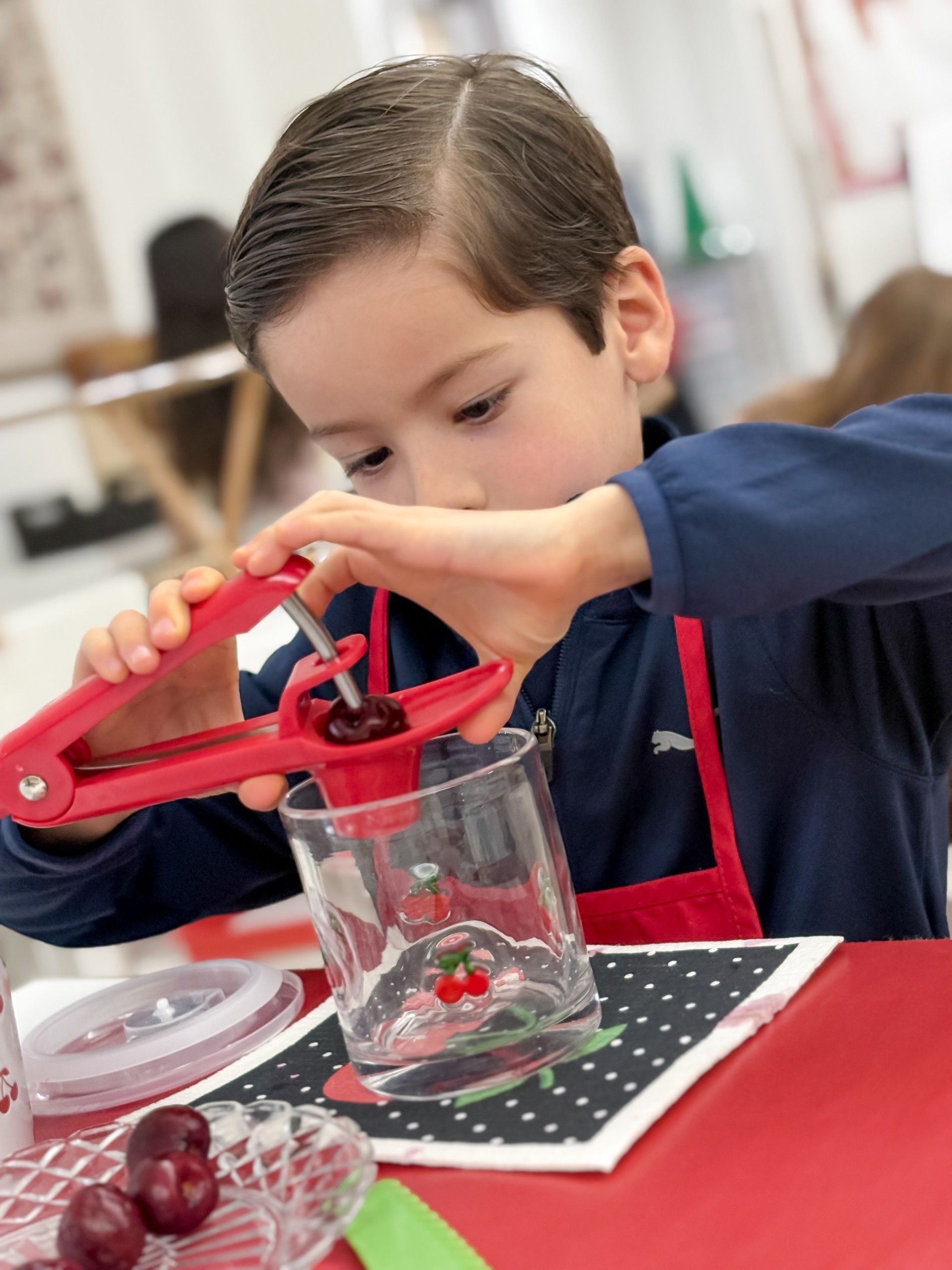 Two boys removing a cherry pit over a glass using a pit remover tool.