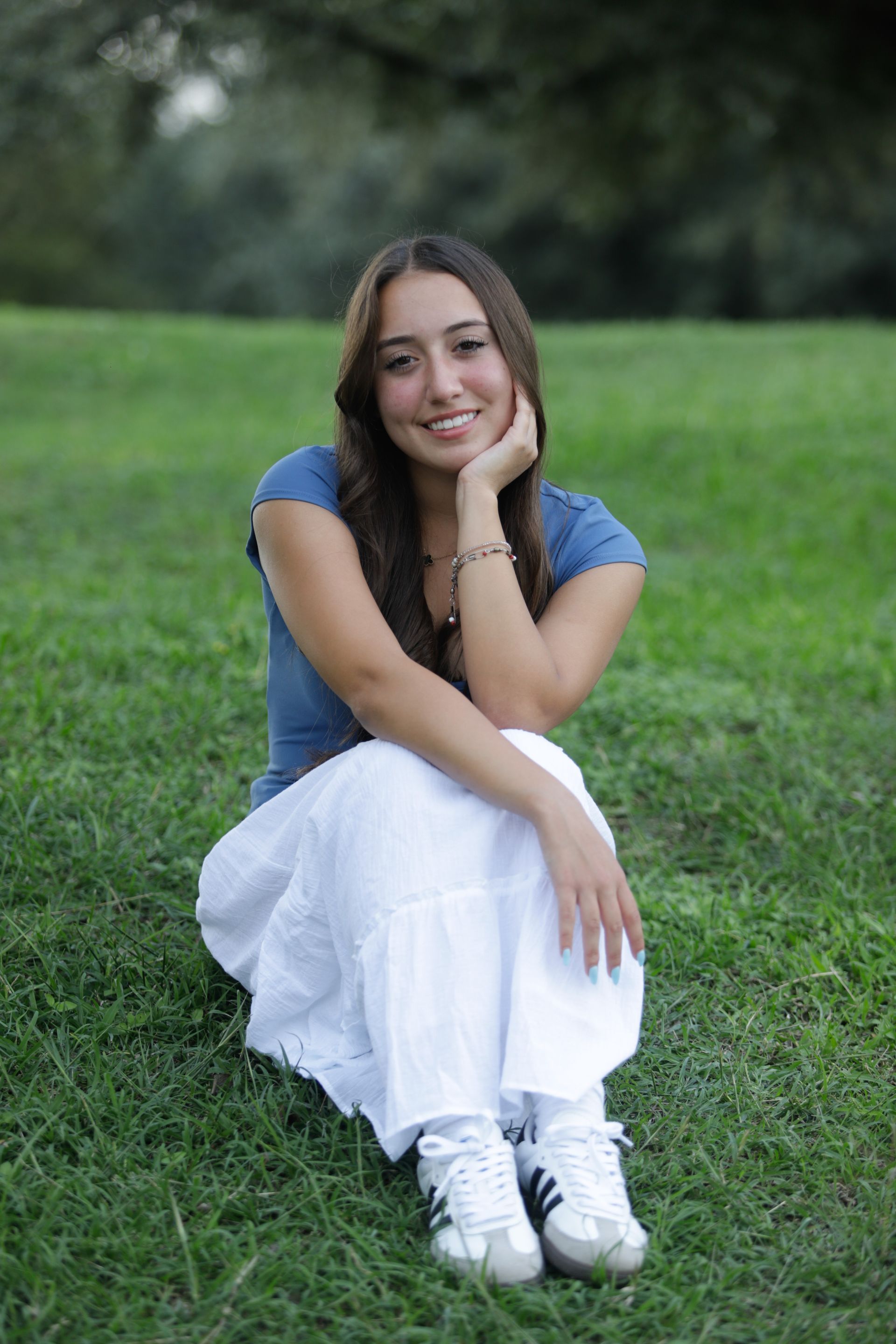 Girl sitting on the lawn with a white skirt and blue t-shirt with her chin in her hand.