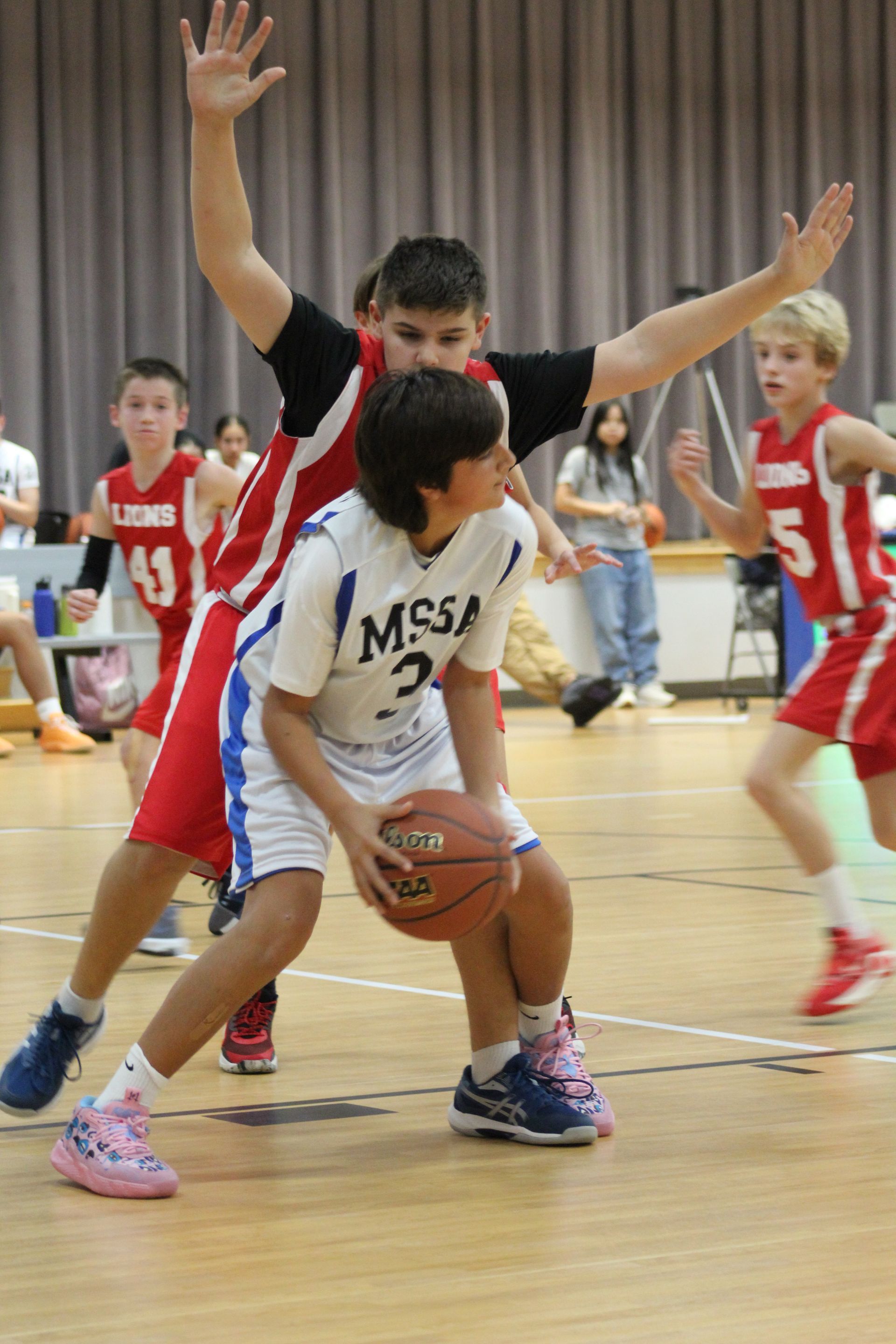 A middle school basketball player has the ball in both hands while being guarded by the opponent.