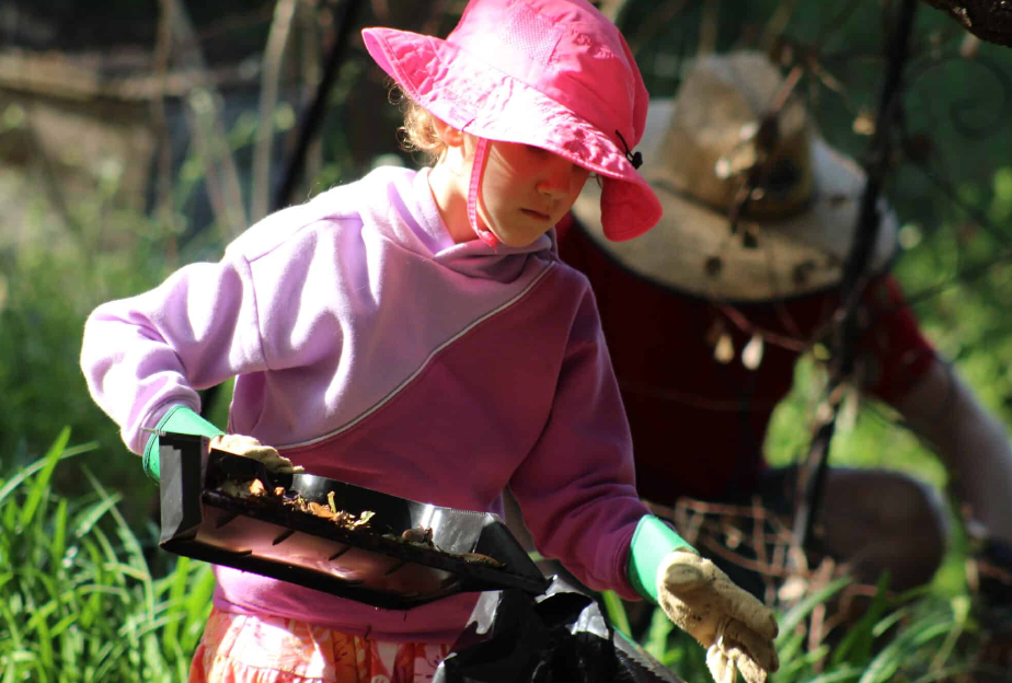 Person wearing a pink hat and gloves handling a small tray outdoors. Another person is visible in the background.