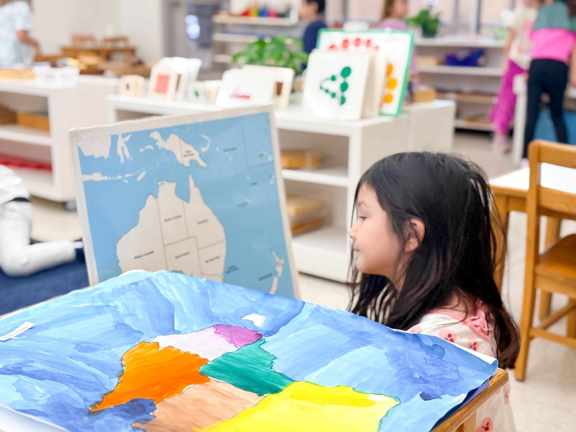 A young girl using watercolors to paint a map of Australia.