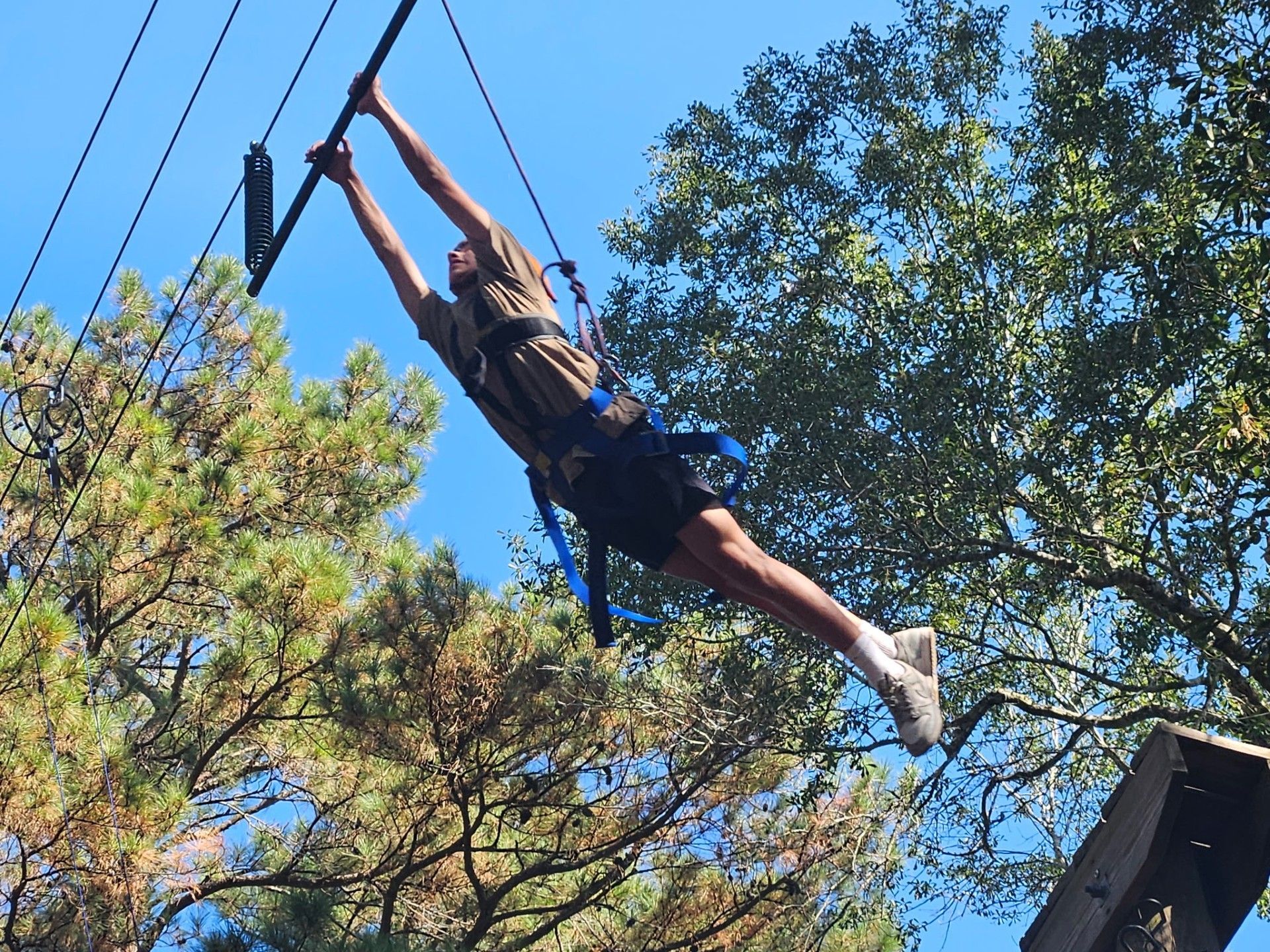 A boy in safety ropes jumps from a platform to a trapeze bar.