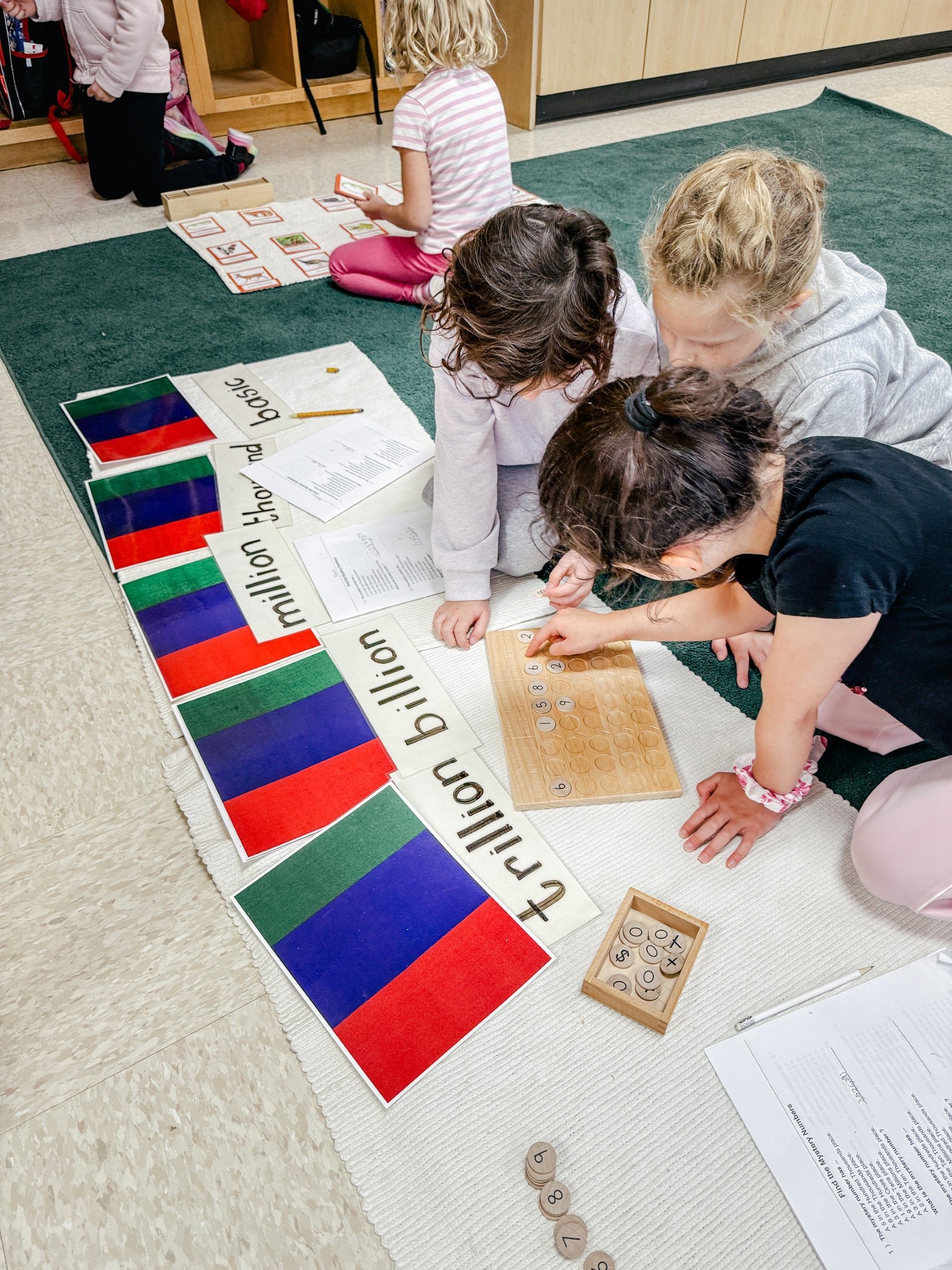 Three girls identifying thousand, million, billion, and trillion using large cards and a wooden pegboard.