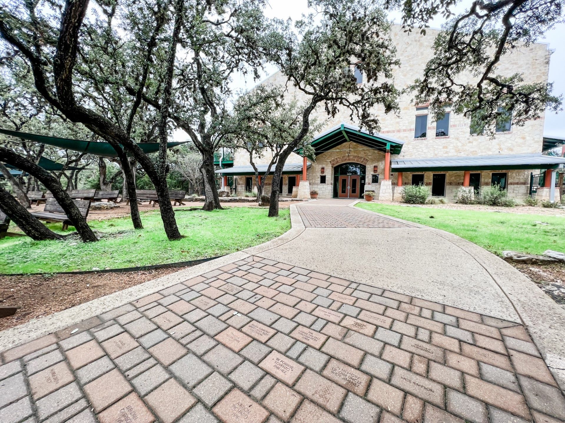 Building exterior with stone walls, brick archway, and double doors, framed by a large tree and brick pathway.