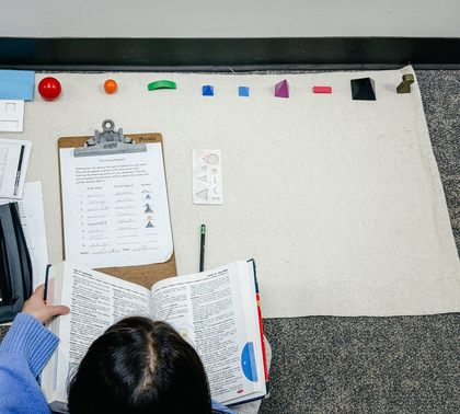 Child using a dictionary and the Montessori grammar symbols to identify nouns, adjectives, and adverbs.