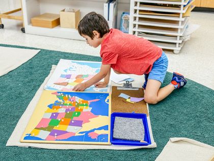 Child using a US puzzle to place the pieces on a large poster of the US, intently focused.