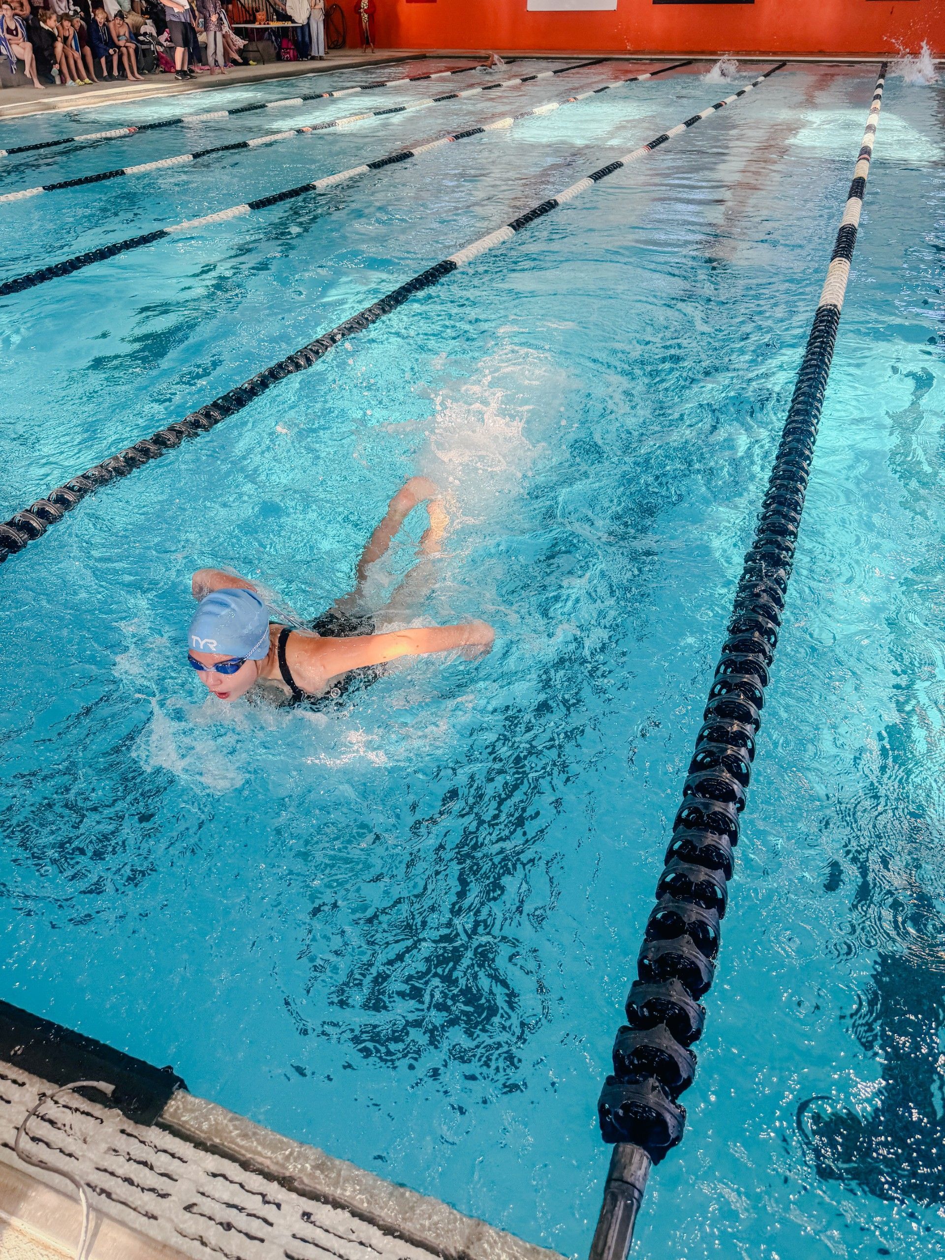 Girl in pool coming up for air as she does the breast stroke.