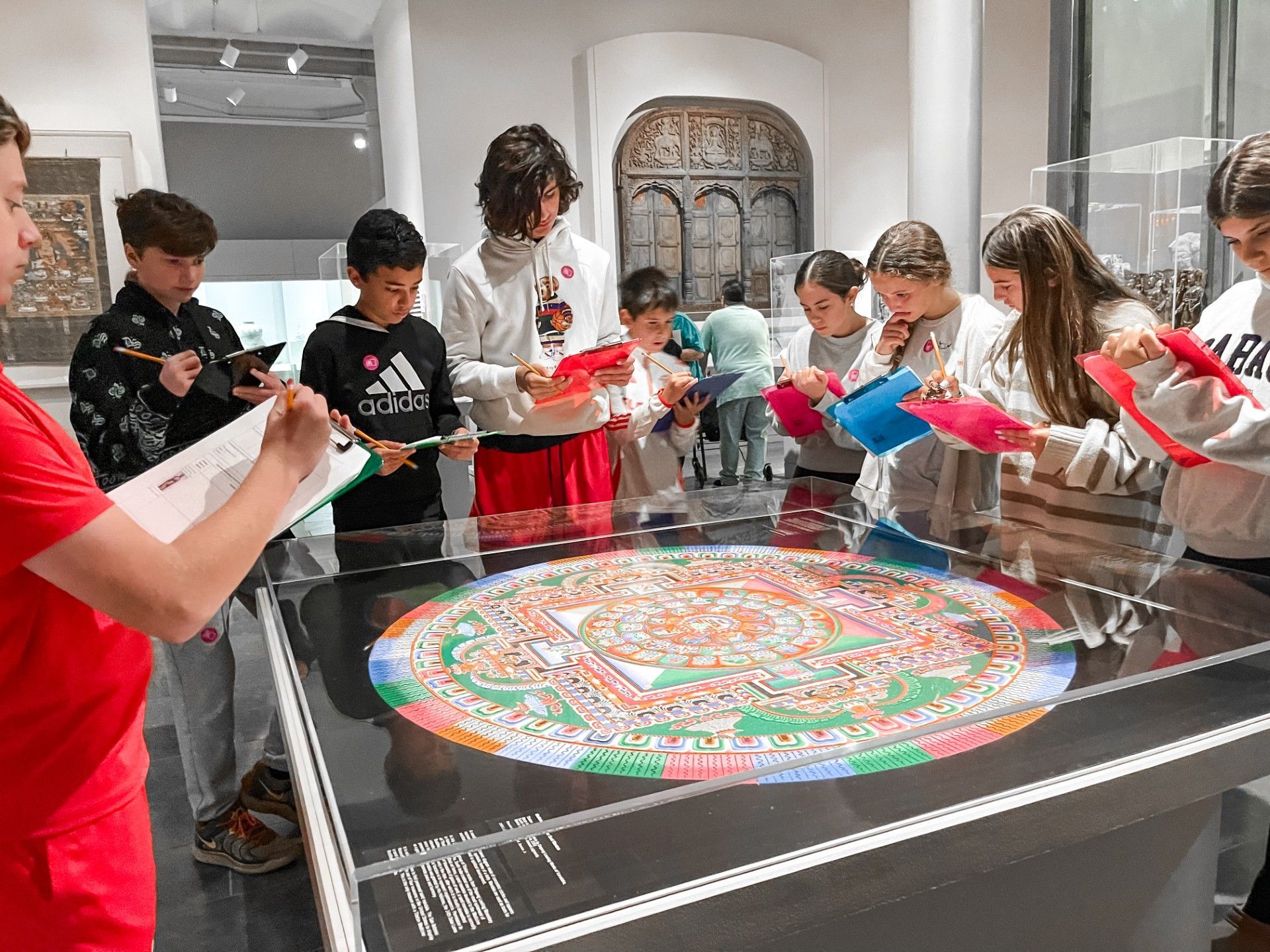 A group of 3 boys and 3 girls around a piece of art at SAMA, taking notes.