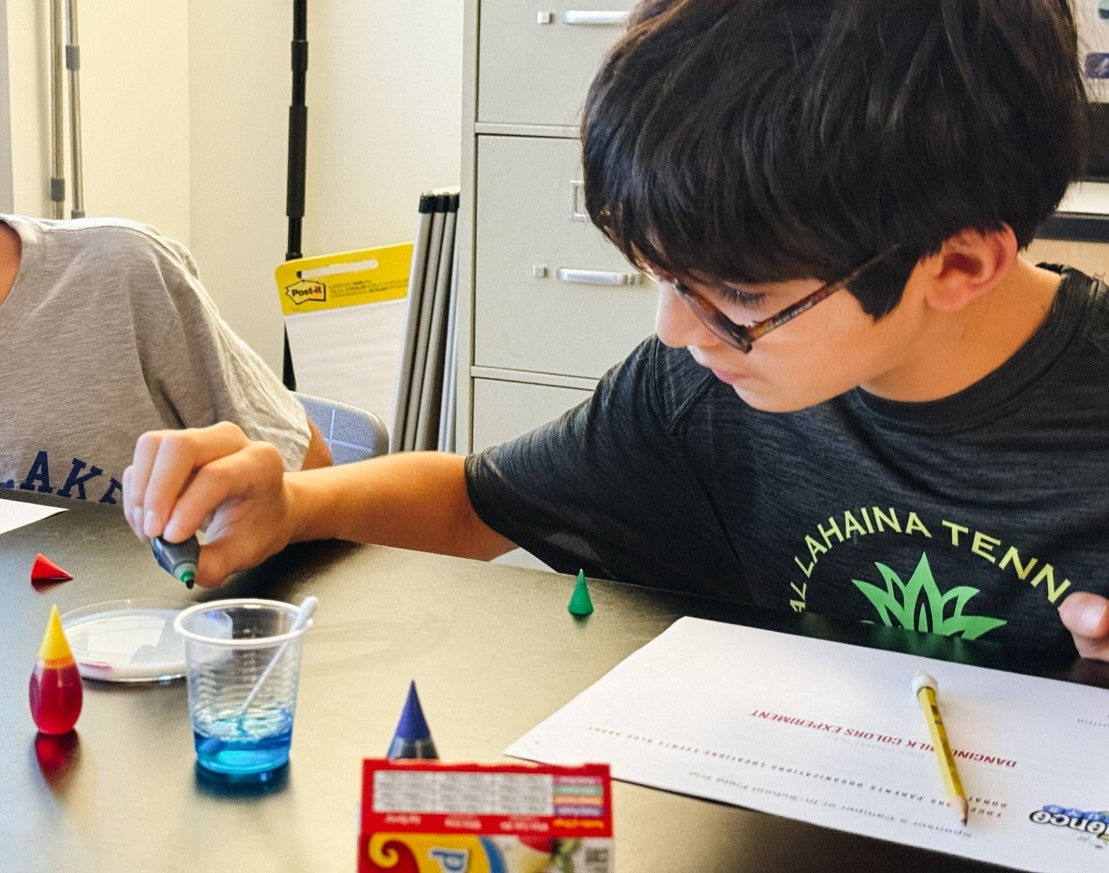 Student adding blue food coloring droplets to milk in a petridish