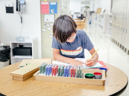 Boy at his desk working with the Montessori tubes on division.