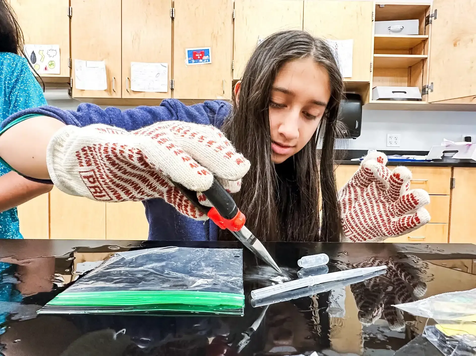 A person wearing gloves using a tool to work on a black surface in a workshop.