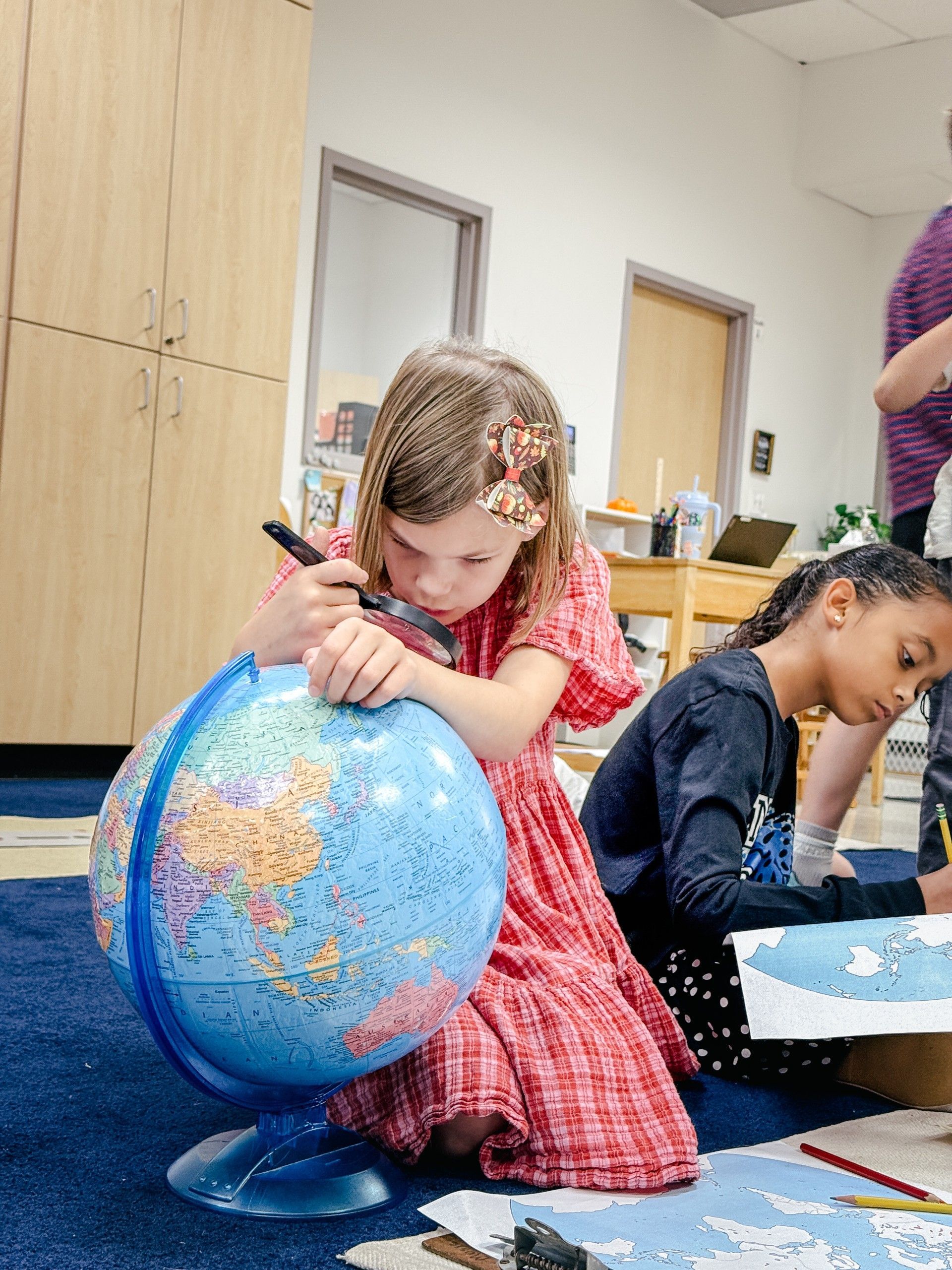Girl in a red dres leaning over a globe looking for a country with a magnifying glass.