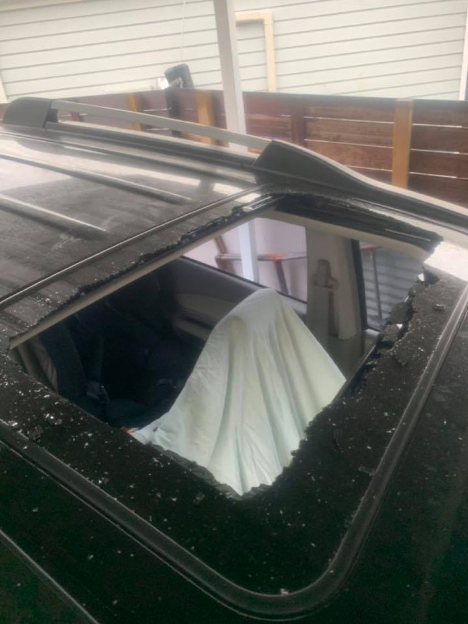 Black car with a broken sunroof, showing damaged glass and a white cloth inside