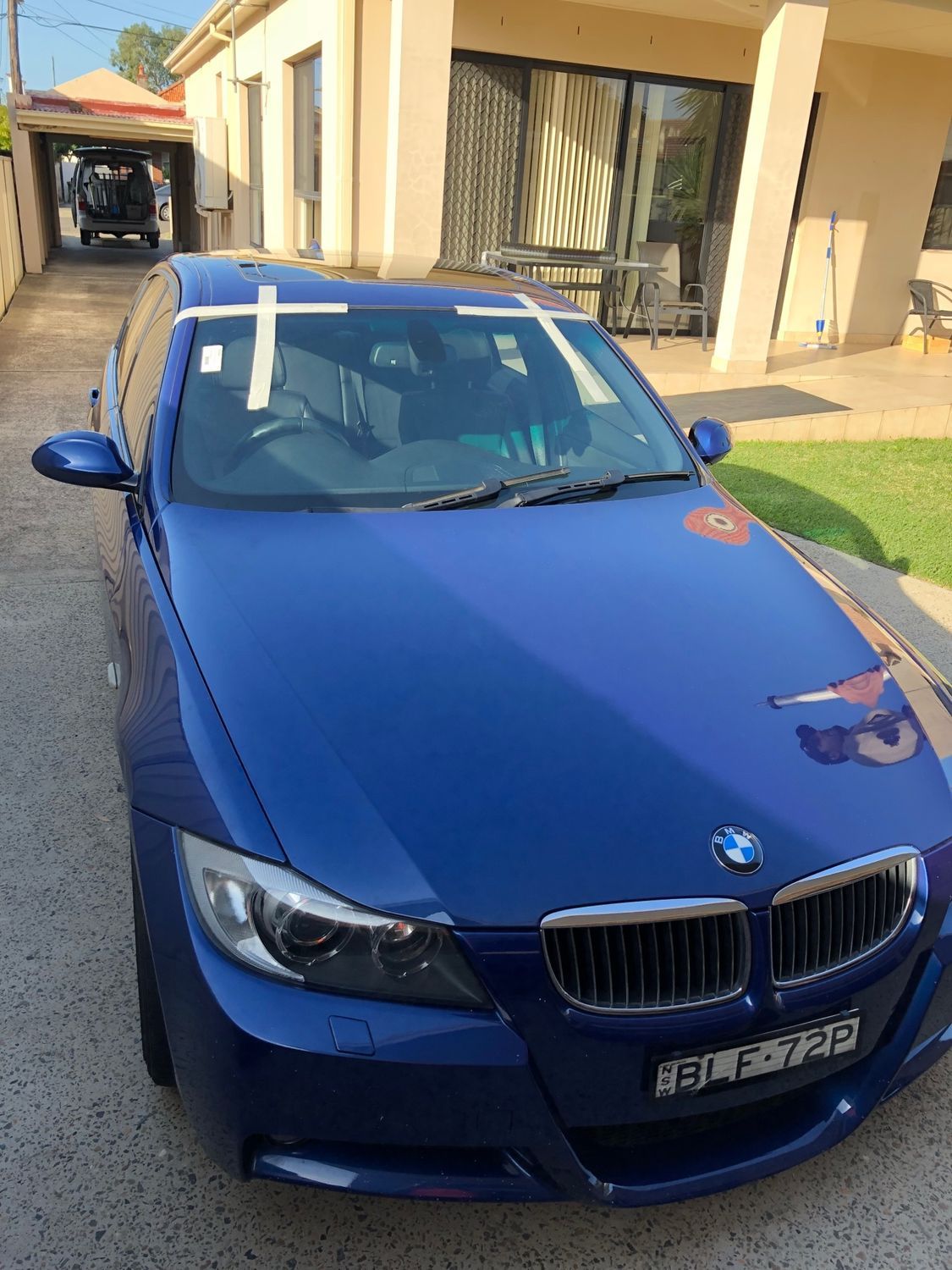 Blue BMW sedan parked in a driveway beside a beige house, front view
