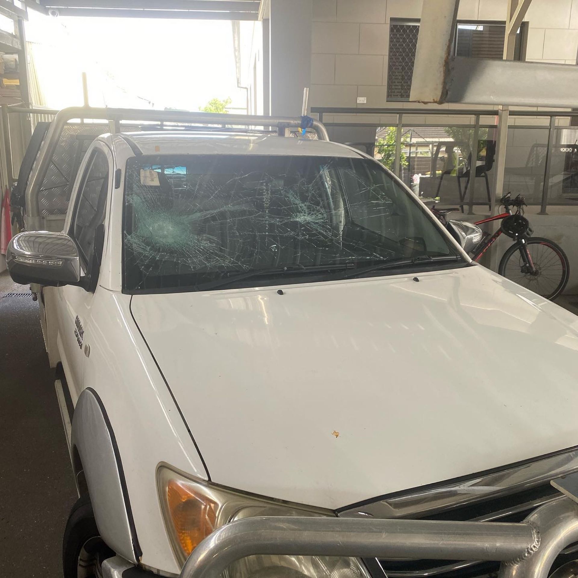 White SUV parked under a covered structure, with a cracked windshield and a bicycle in the background.