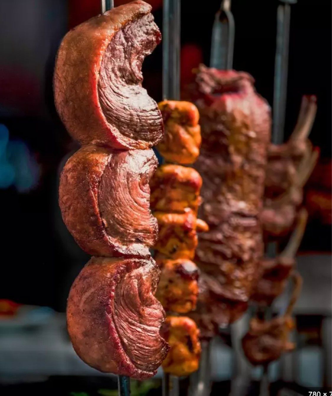 A bunch of meat is hanging from skewers on a rack.