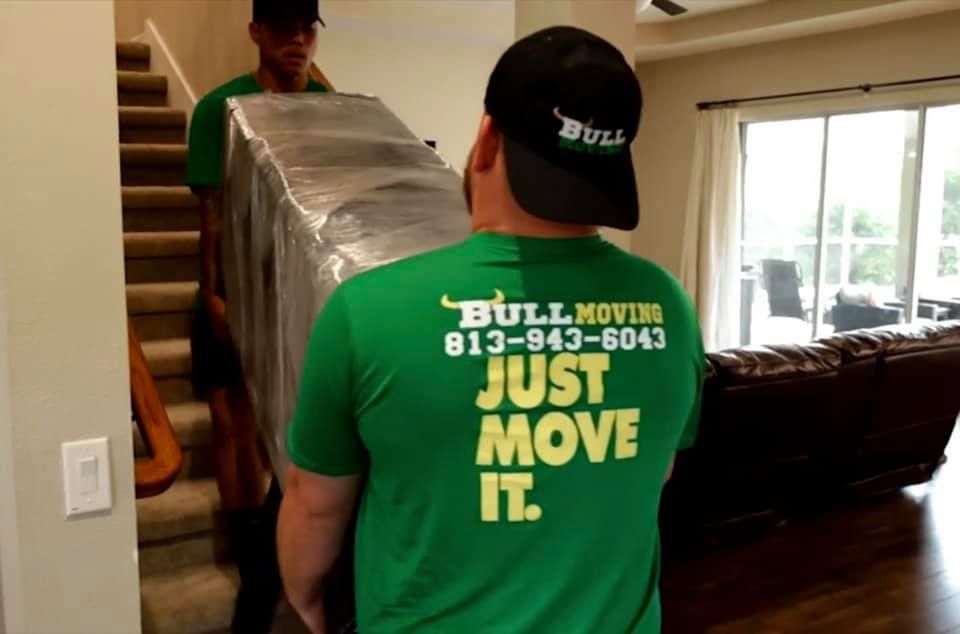 two movers carrying a large wrapped item up a staircase
