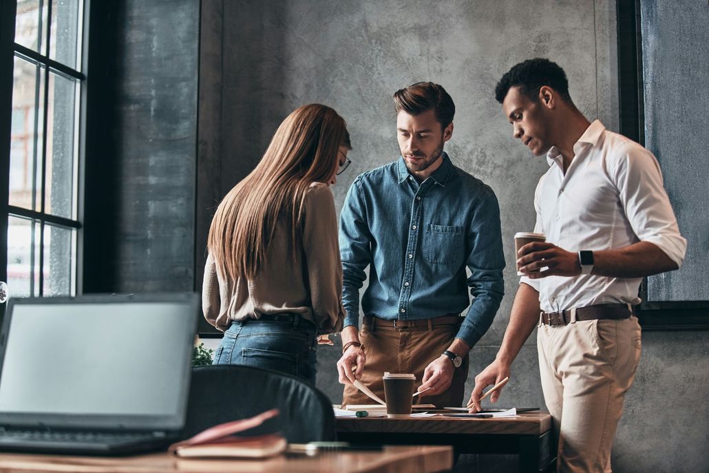 Three little girls are sitting on the grass near the water.