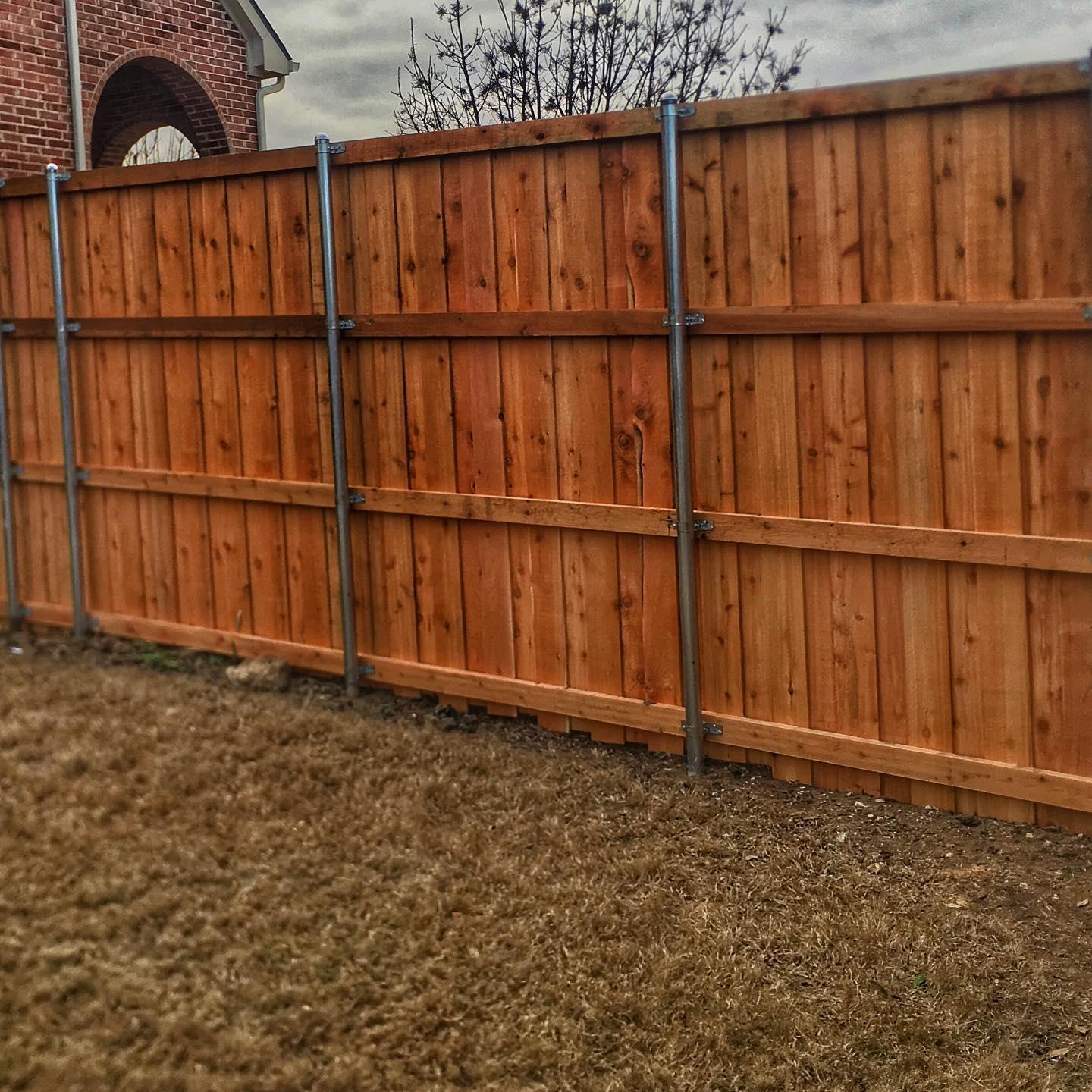 A wooden fence in a backyard with a brick building in the background