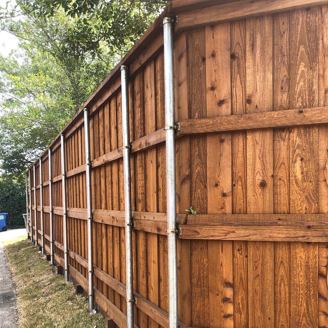 A wooden fence with metal poles and trees in the background.