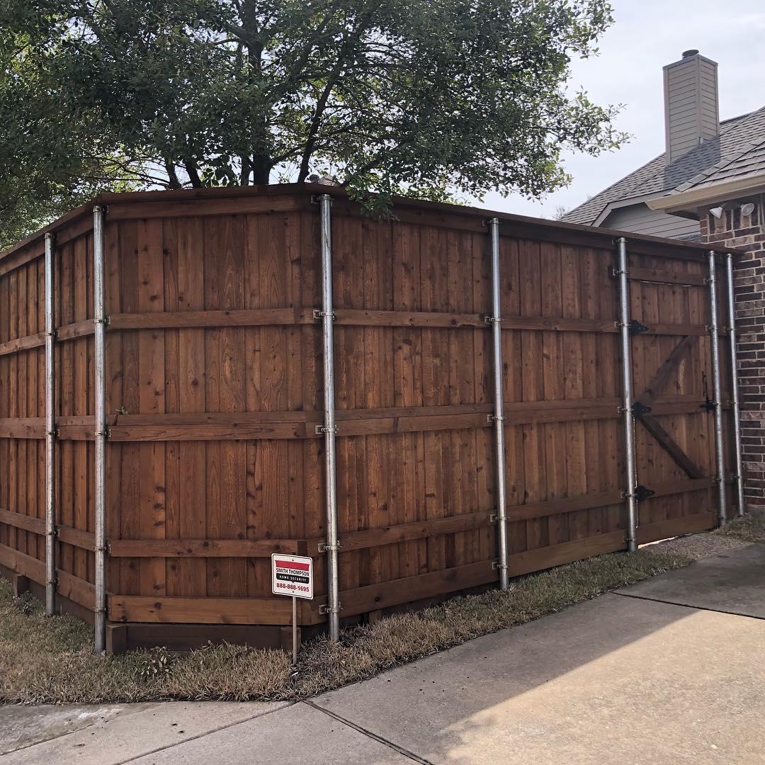 A large wooden fence is sitting on the side of a road next to a house.