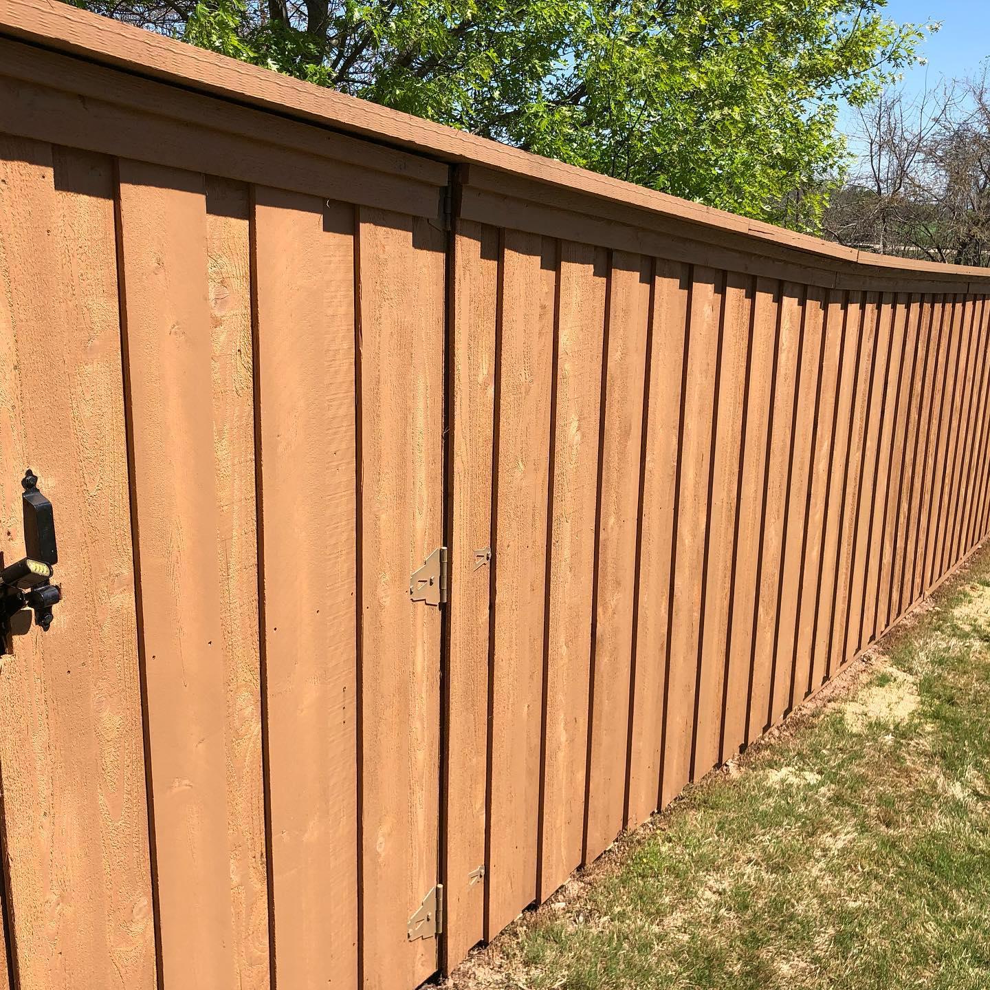 A brown wooden fence is surrounded by grass and trees