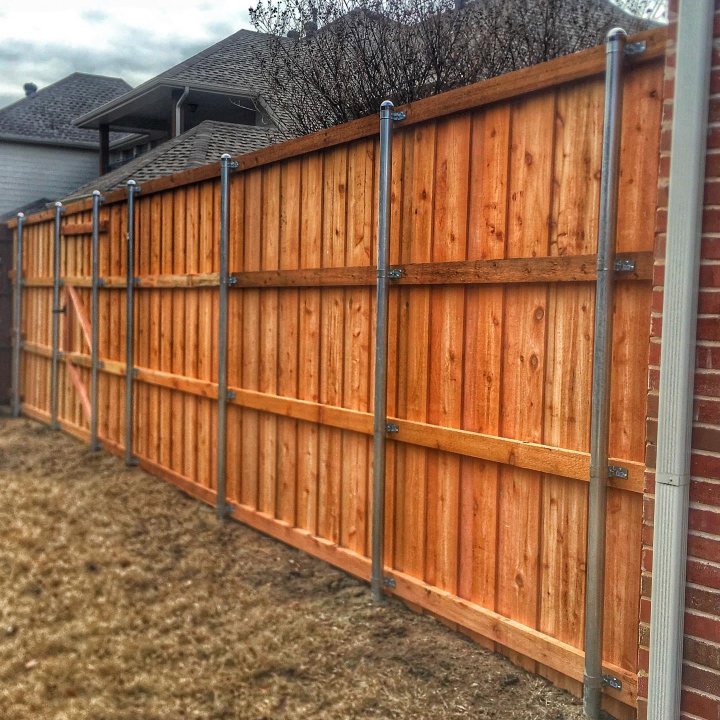 A wooden fence is surrounding a brick house in a backyard.