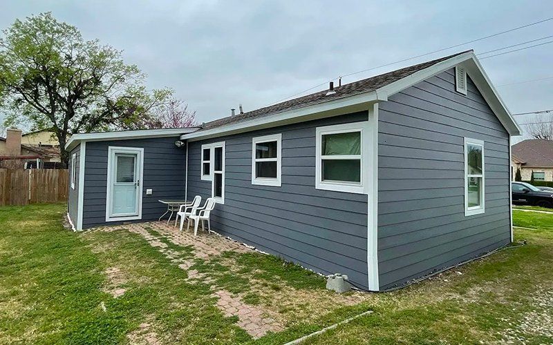 A small gray house with white trim is sitting on top of a lush green lawn.