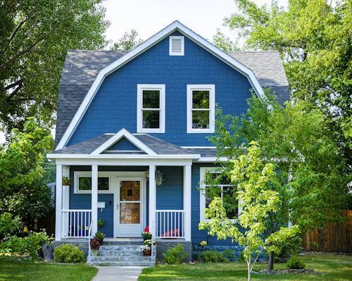 Blue two-story house with white trim, front porch, and a tree-lined yard