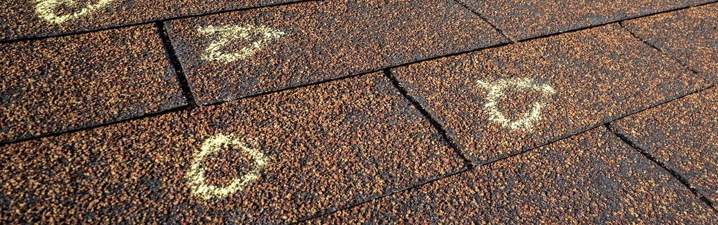 Brown asphalt roof shingles with hail damage, showing areas of missing granules.