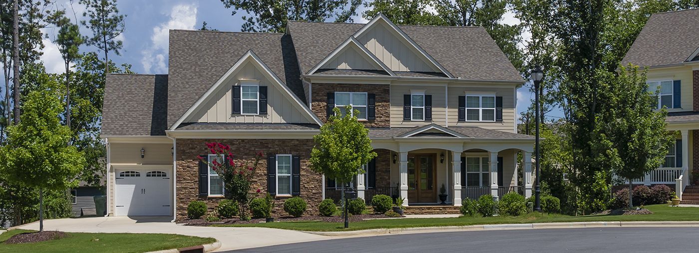 Two-story brick and siding house with a porch and shutters, surrounded by trees and a driveway.